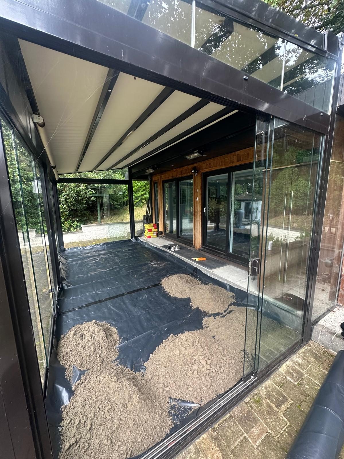 Screed heaped on the visqueen membrane inside the glass summer room, ready to spread