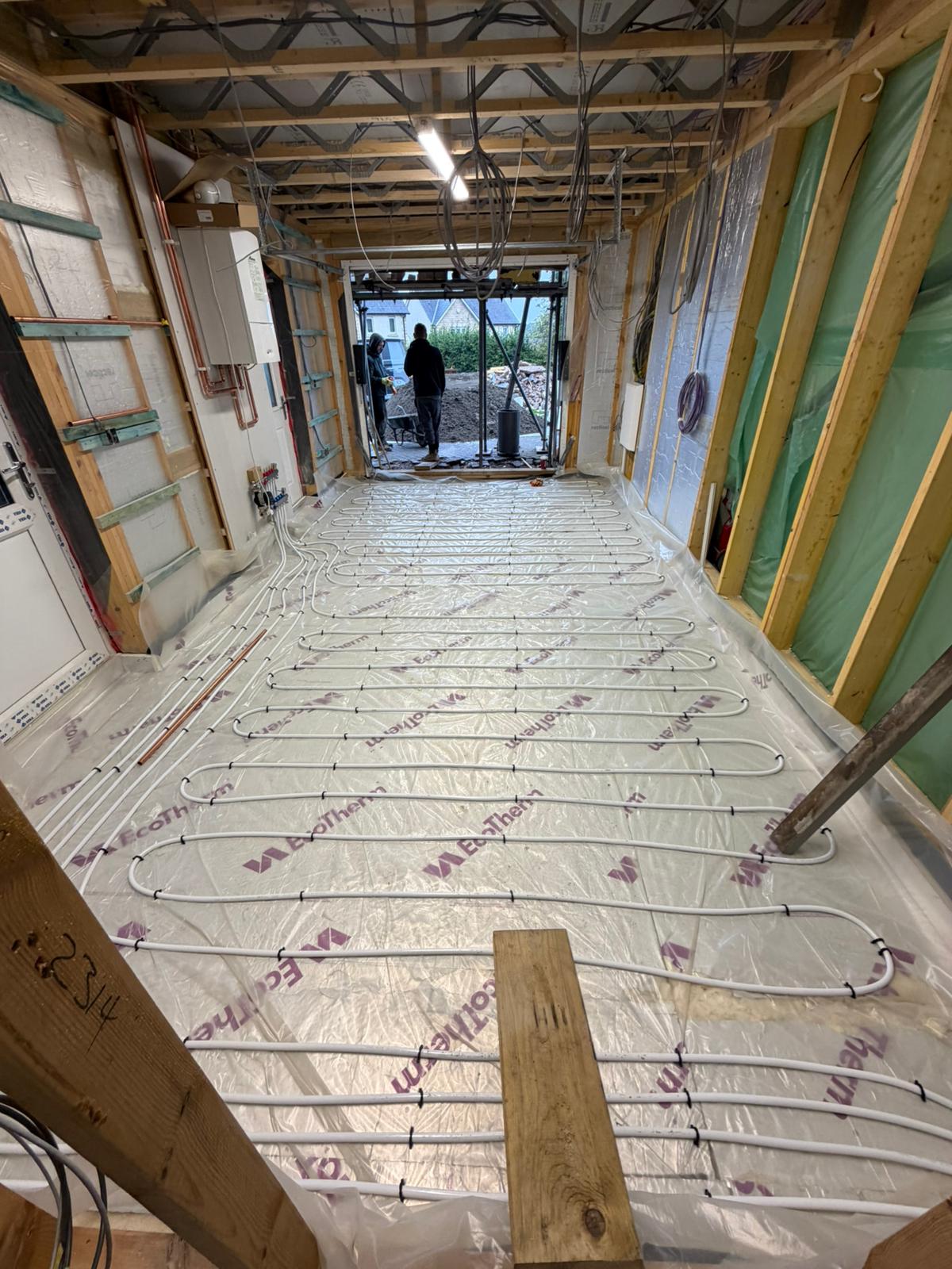Underfloor heating loops clipped down over the floor insulation, with the doorway open to the site outside